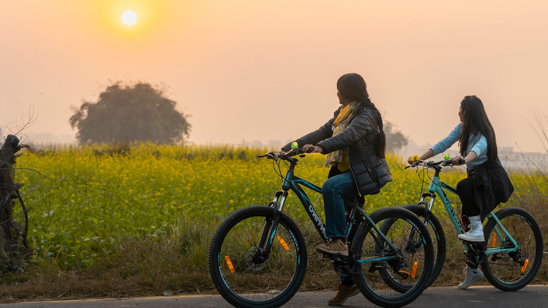 Two cyclists on a country lane past fields at sunrise near Lumbini